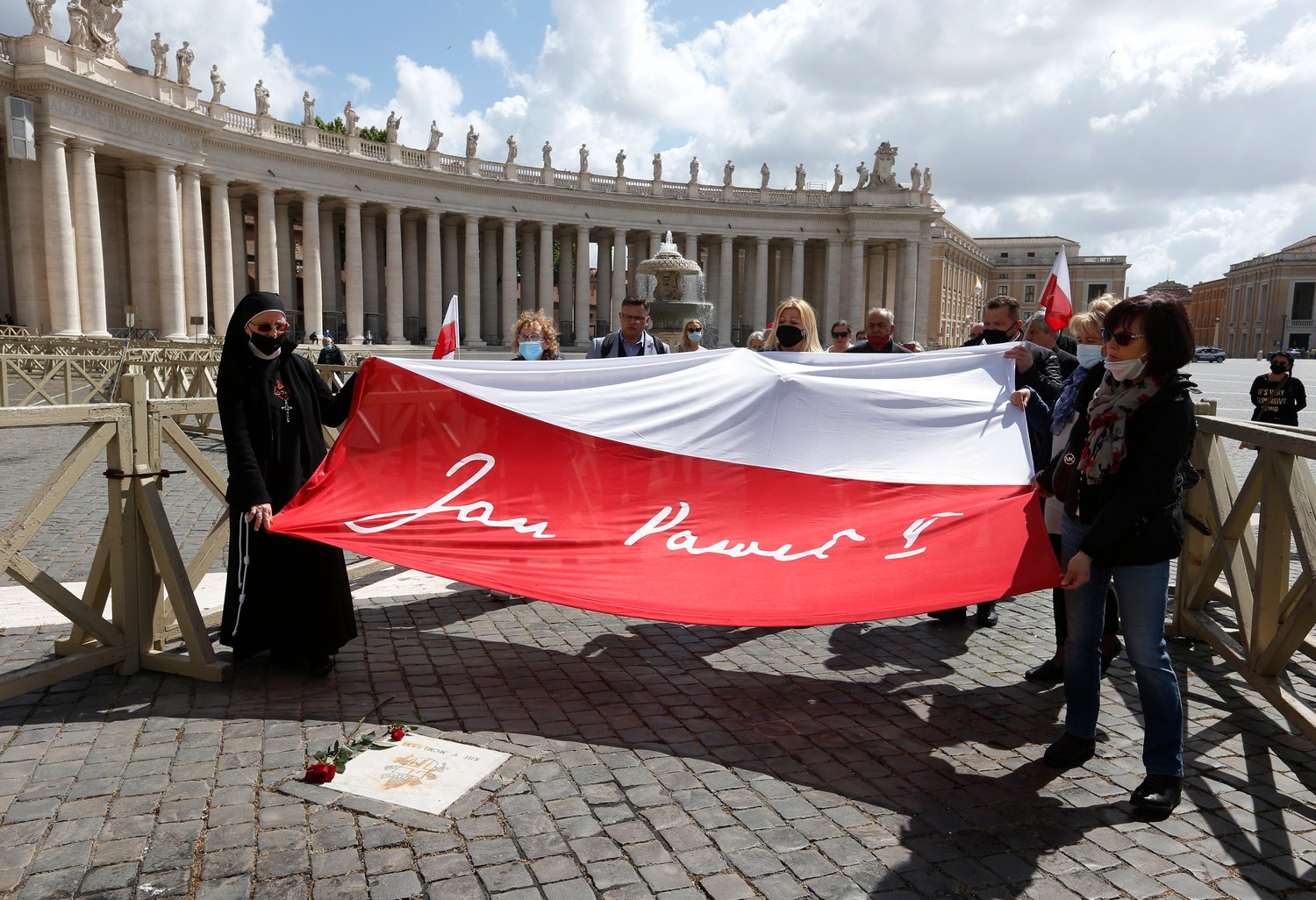 People carry a flag with the name of St. John Paul II over the spot of the May 13, 1981, assassination attempt against the Polish pope, in St. Peter’s Square at the Vatican May 13, 2021. Cardinal Stanislaw Dziwisz, the former secretary of St. John Paul II, and a small group of Catholics gathered in the square to mark the 40th anniversary of the shooting.